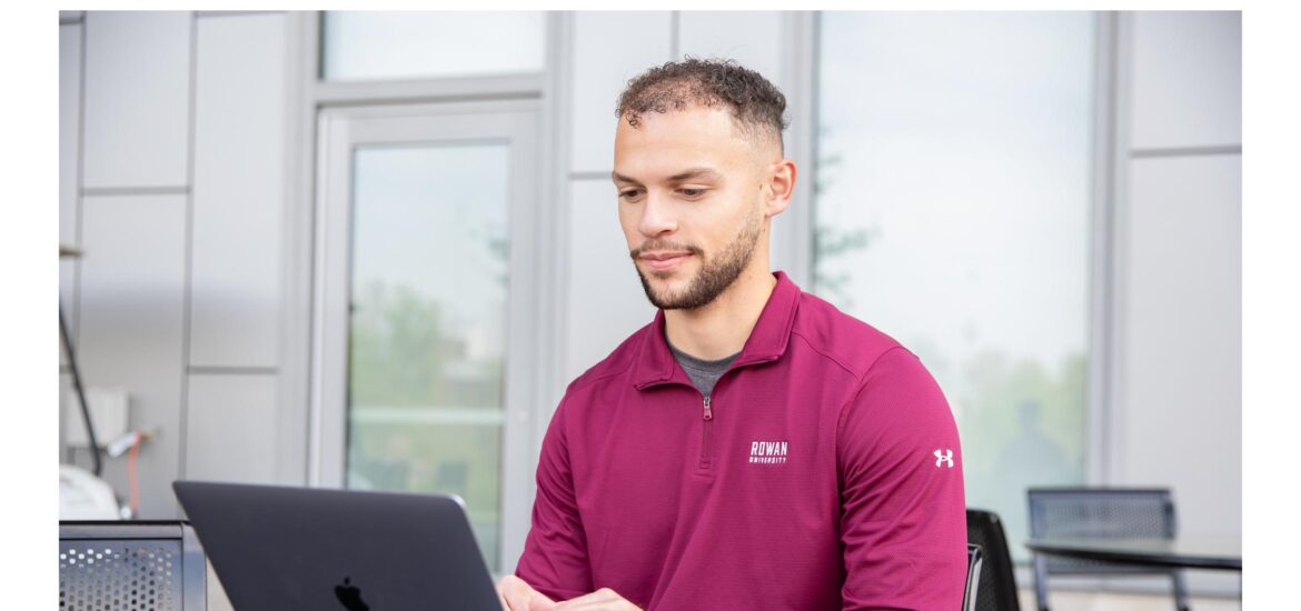 Student using laptop outdoors wearing Rowan University apparel, symbolizing how to become an EdTech professional and exploring EdTech programs