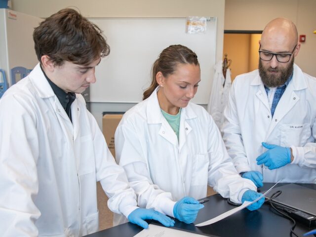 A Rowan nurse educator illustrates a point for two students in a lab.