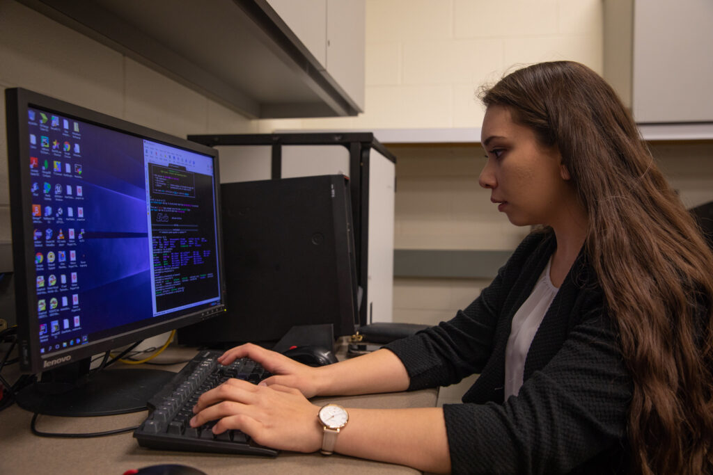 Student sitting at computer completing online computer information systems degree coursework.
