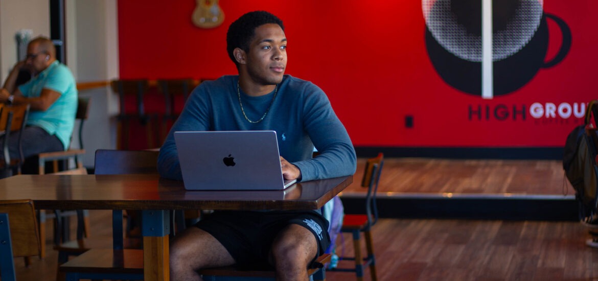 Student sitting down in coffee shop completing online coursework for bachelor of science in business administration program