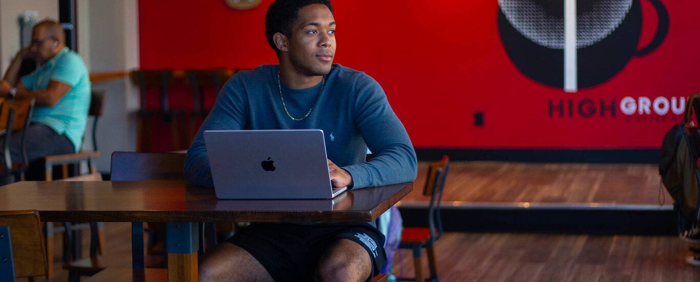 Student sitting down in coffee shop completing online coursework for bachelor of science in business administration program.