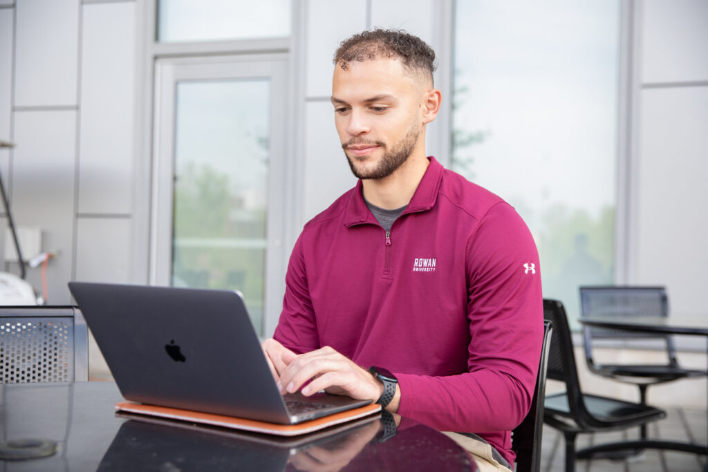Student completing coursework on laptop for bs in business administration program outside at table