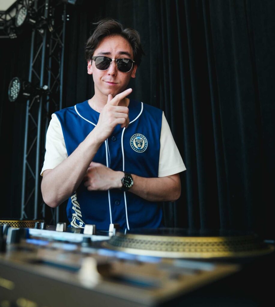 JT smiles for a portrait while wearing sunglasses and behind a DJ turntable. 