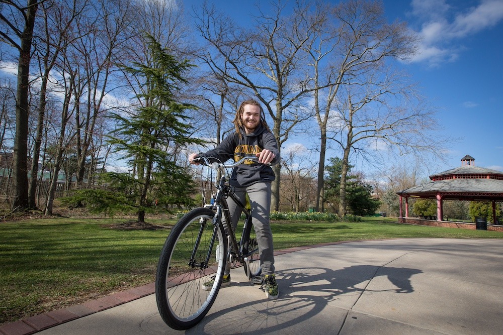 Student sits on a bike on the wide sidewalk leading to Holly Pointe Commons. 