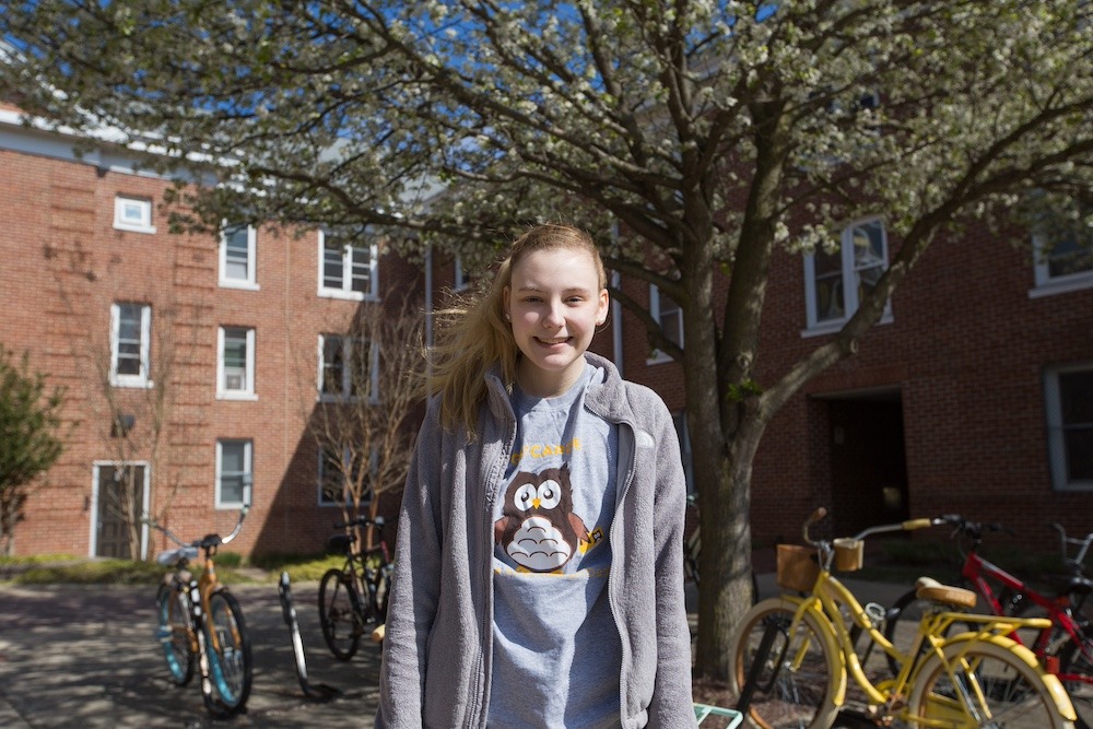 Wearing a cutesy owl shirt with a jacket, a first year student stands outside of her dorm on a crisp day. 
