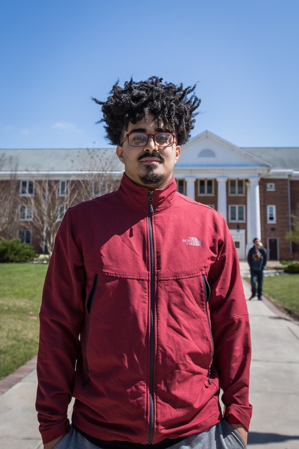 Rowan University student wears red jacket while standing in a portrait pose in front of Chestnut. 