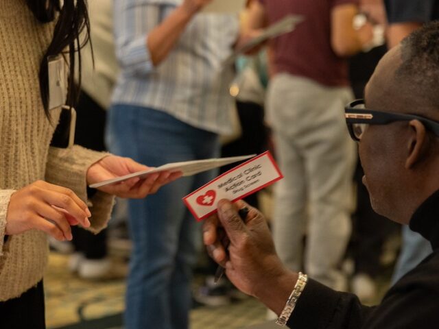 A close up of a man at a table handing a law and justice student a card that says medical clinic access card.