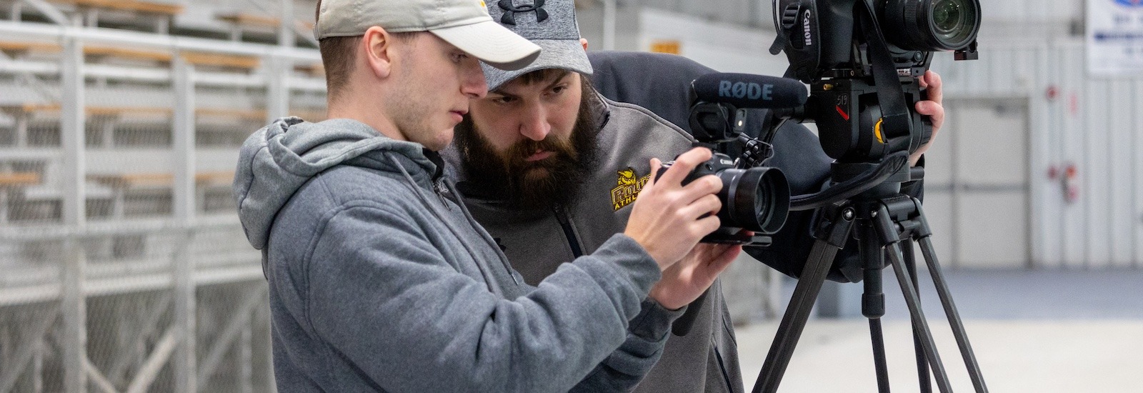 A Rowan radio tv film major works with a supervisor in the field looking at a camera.