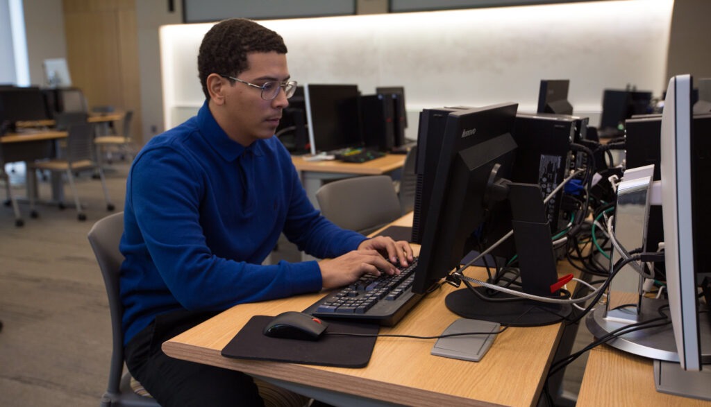 Student working on a desktop computer in a classroom, showing how online MBA coursework translates into career-ready skills.
