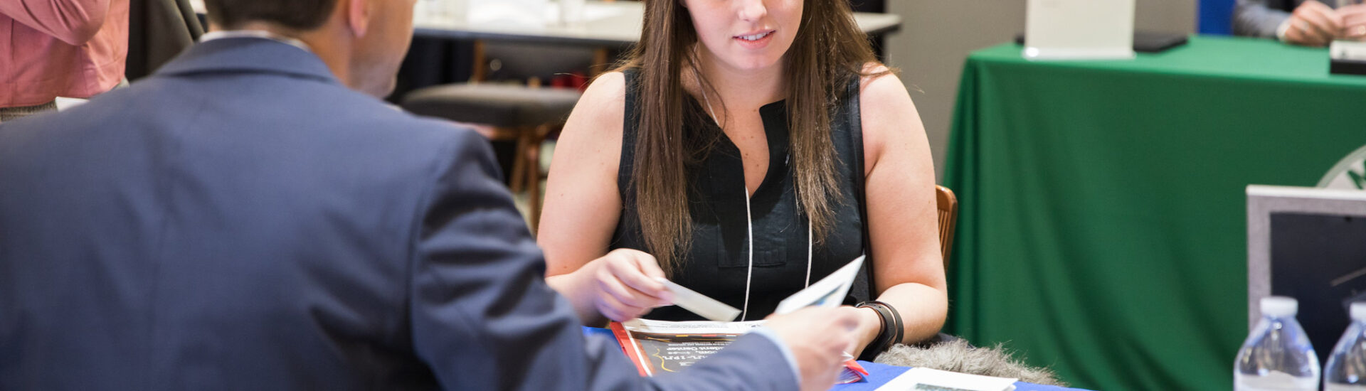 Online MBA student speaking with a recruiter at a career fair table, highlighting how networking helps market your MBA degree.