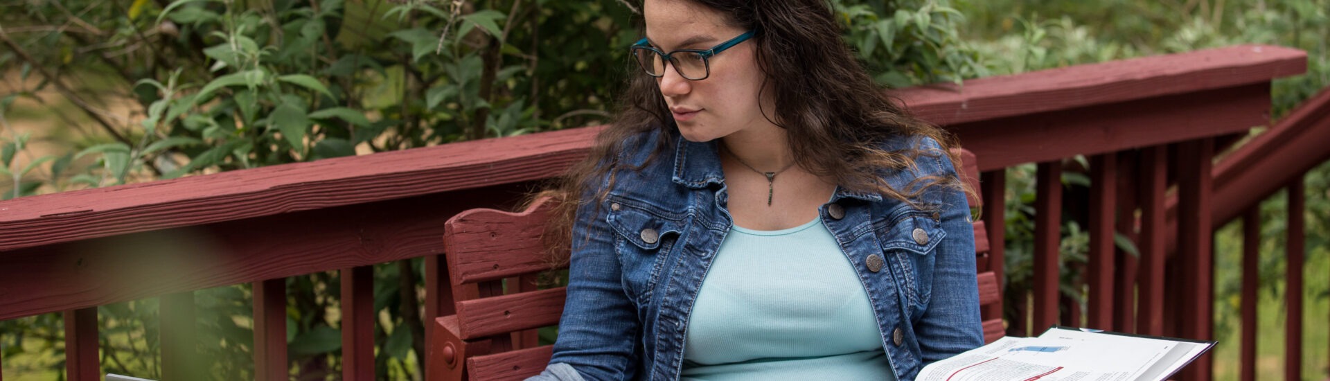 Adult student studying online outdoors with laptop and textbook, balancing education and family life.