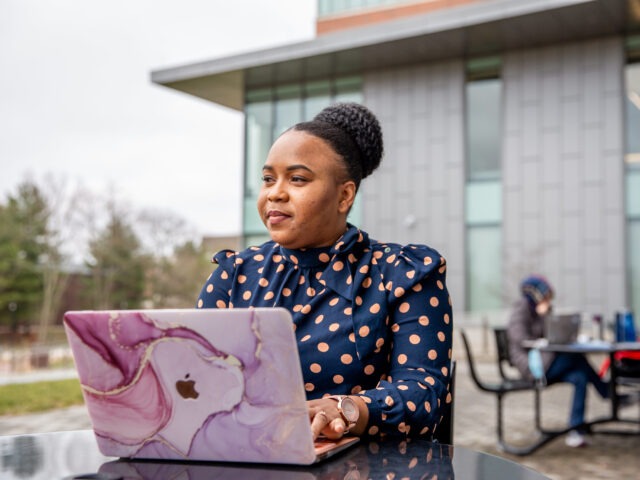 Online MBA student studying outdoors on Rowan University’s campus with a laptop.