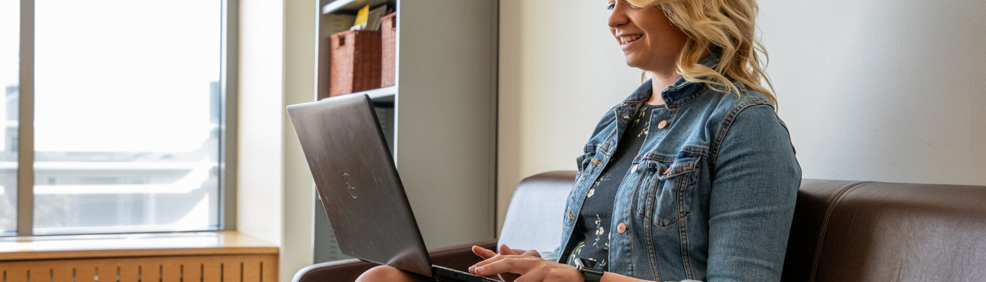 Smiling student working on her laptop from home while earning an online master’s in education degree.