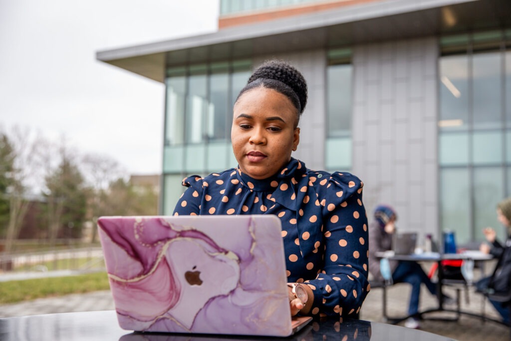 Online MBA student completing coursework on laptop sitting down outside.