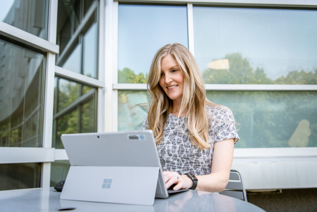 Student sitting outside on laptop completing coursework for online classes.