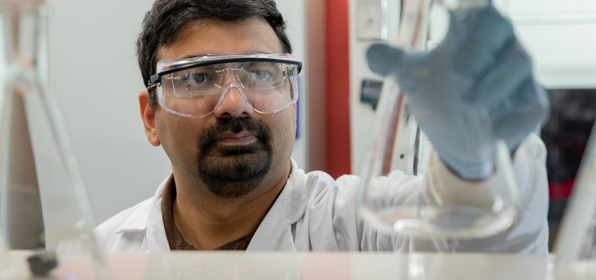 A Rowan student researcher examines a beaker he's holding in the air.
