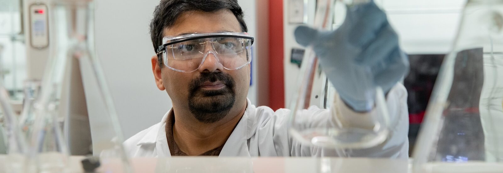 A Rowan student researcher examines a beaker he's holding in the air.
