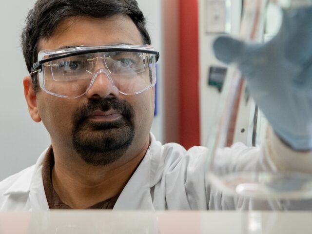 A Rowan student researcher examines a beaker he's holding in the air.