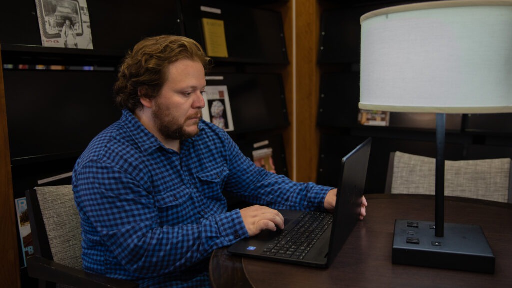 Student sitting at a table on laptop completing coursework for online classes.