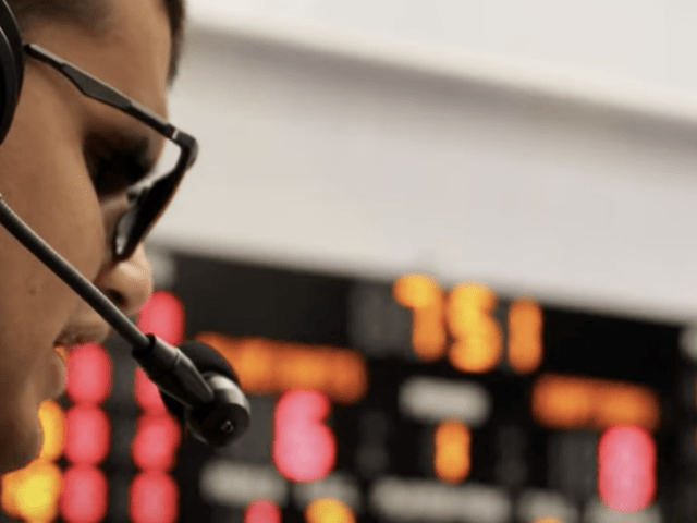A side profile of ports communication and media major Allan Wylie as he wears a headset on the sidelines of a basketball game doing sports commentary.