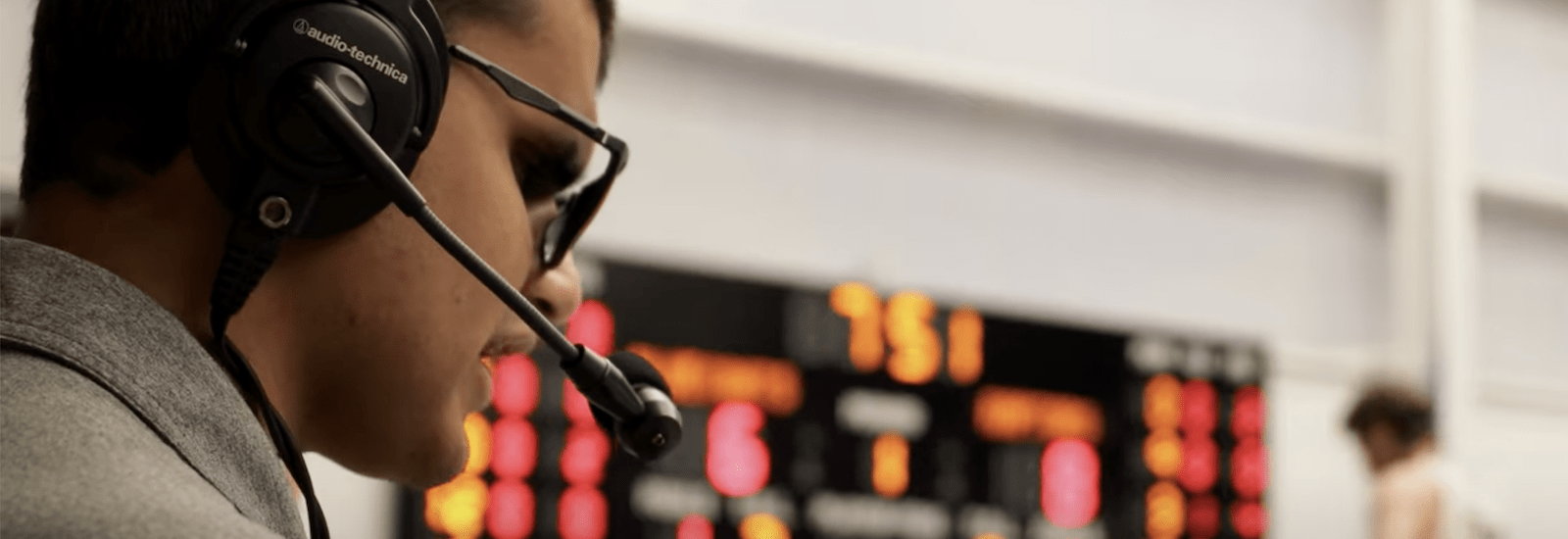 A side profile of ports communication and media major Allan Wylie as he wears a headset on the sidelines of a basketball game doing sports commentary.