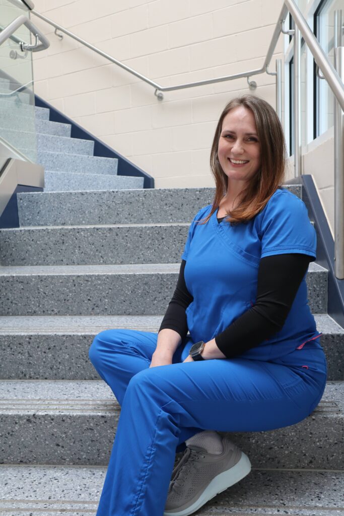 Student in scrubs sitting on stairs smiling with confidence after completing her BSRT degree.