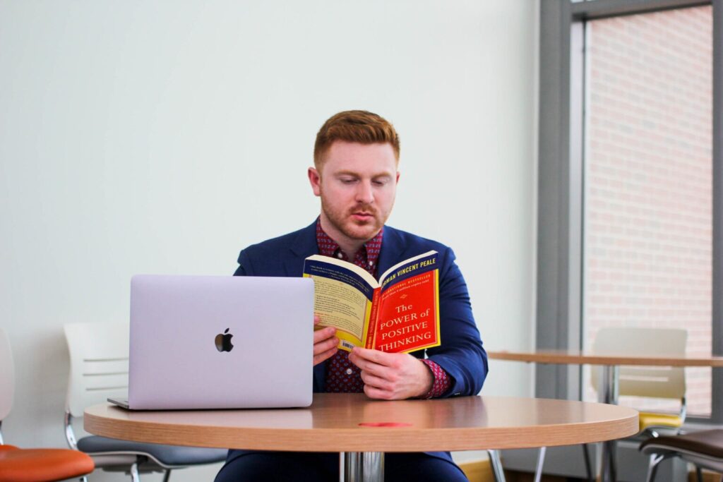 Student in professional attire reading The Power of Positive Thinking with a laptop, highlighting career readiness after a psychology bachelor’s degree online.