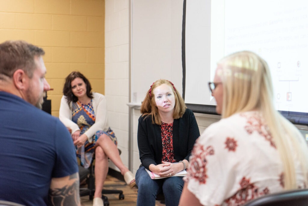 A small group setting in an older building with a projector screen lighting up behind the people, a the leader with an MSW leads a discussion.