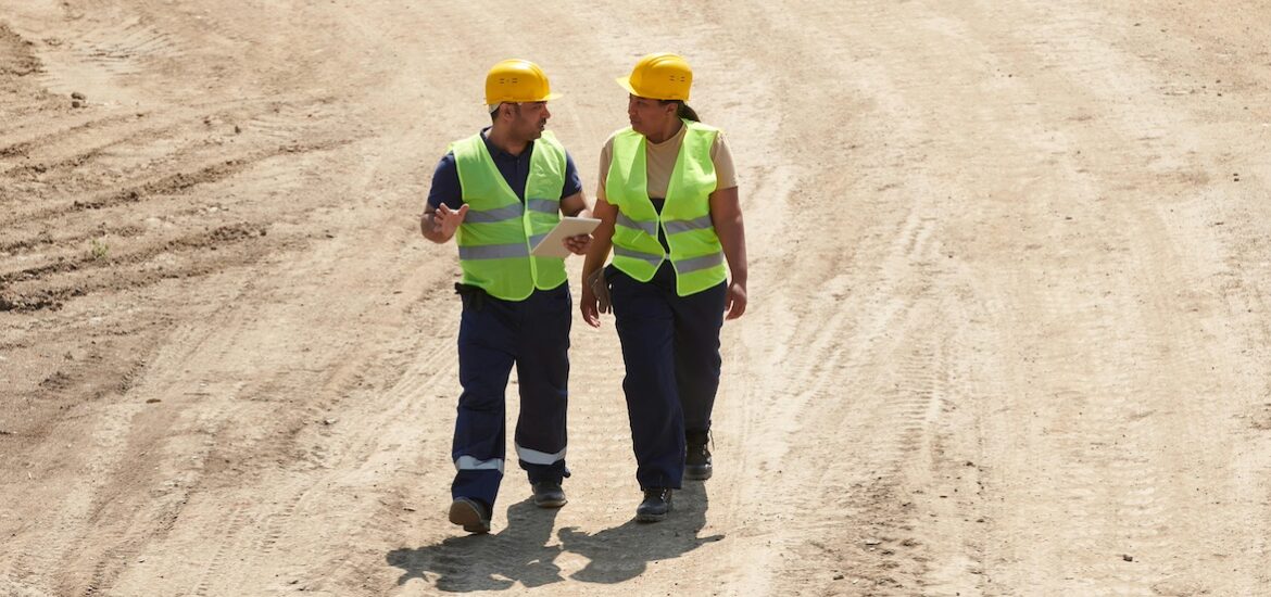 Two construction managers walk through a construction site surrounded by open dirt.