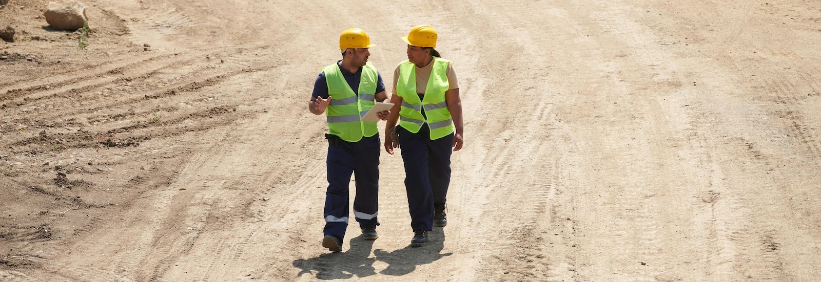 Two construction managers walk through a construction site surrounded by open dirt.