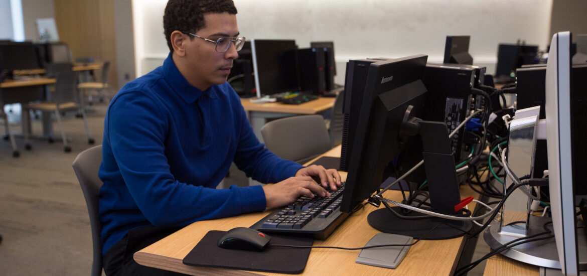 Student working on a desktop computer in a lab, developing technical skills for an online data analytics degree.