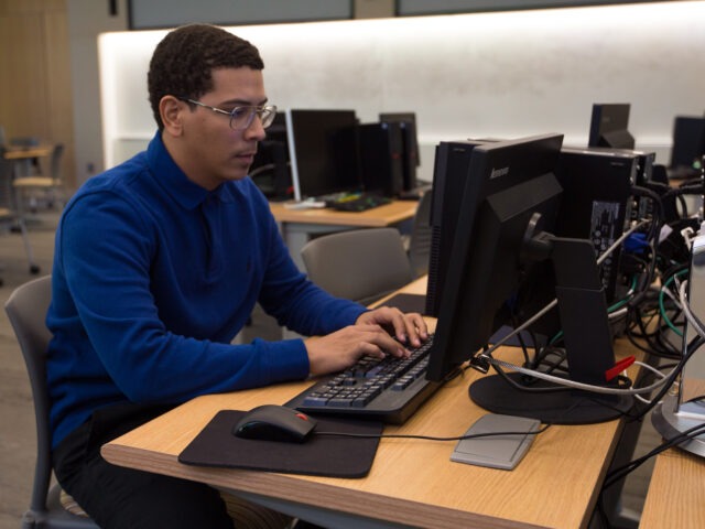 Student working on a desktop computer in a lab, developing technical skills for an online data analytics degree.