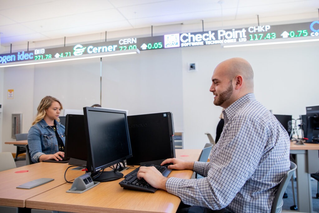 MBA students working at computers with a stock market ticker, representing careers in finance, business analysis and management.