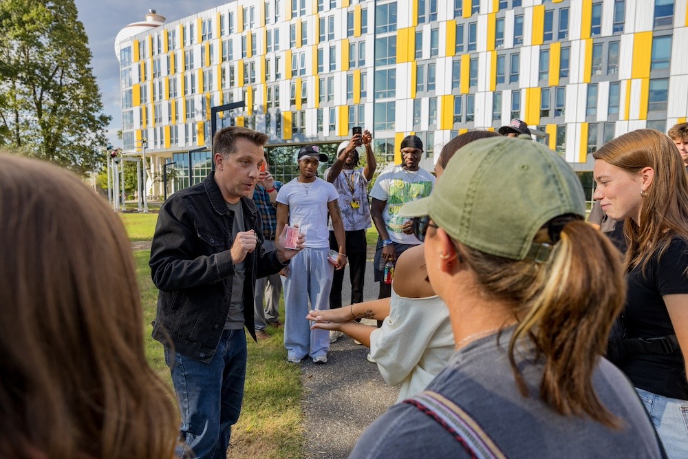 Magician and Rowan marketing alumnus David Corsaro performs a card trick as he is circled by students outside of Holly Pointe Commons residence hall. 
