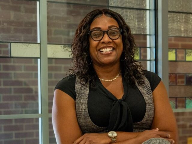 Online M.Ed. in Teacher Leadership student sitting down smiling with arms folded.