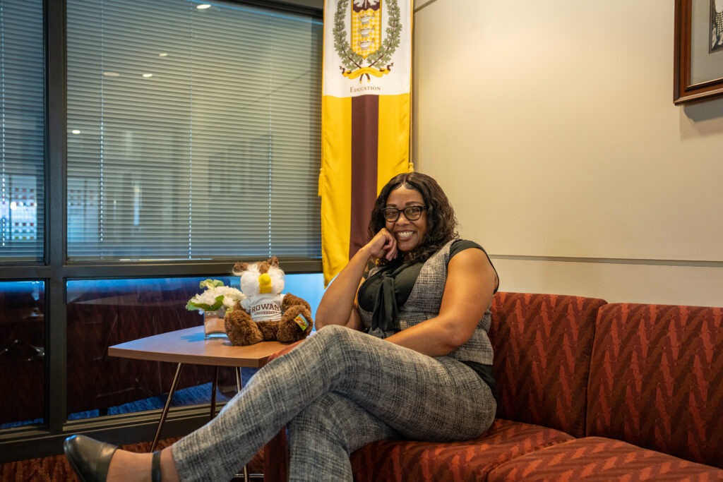 Online M.Ed. in Teacher Leadership student sitting on couch in education suite smiling with hand on cheek.