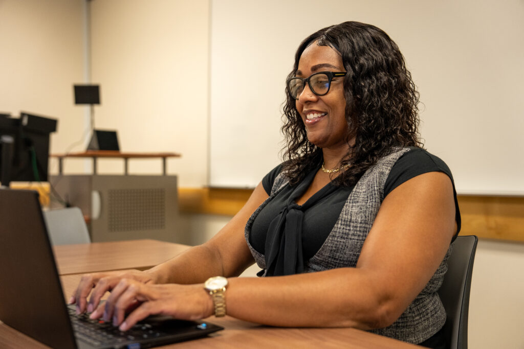 M.Ed. in Teacher Leadership student completing online coursework sitting down on laptop.
