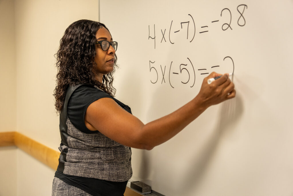 Online M.Ed. student in action in the classroom writing a math problem on the whiteboard.