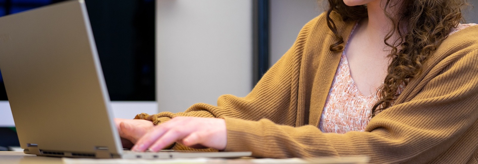 A close up of hands working on a laptop as the student wears a light brown cardigan.