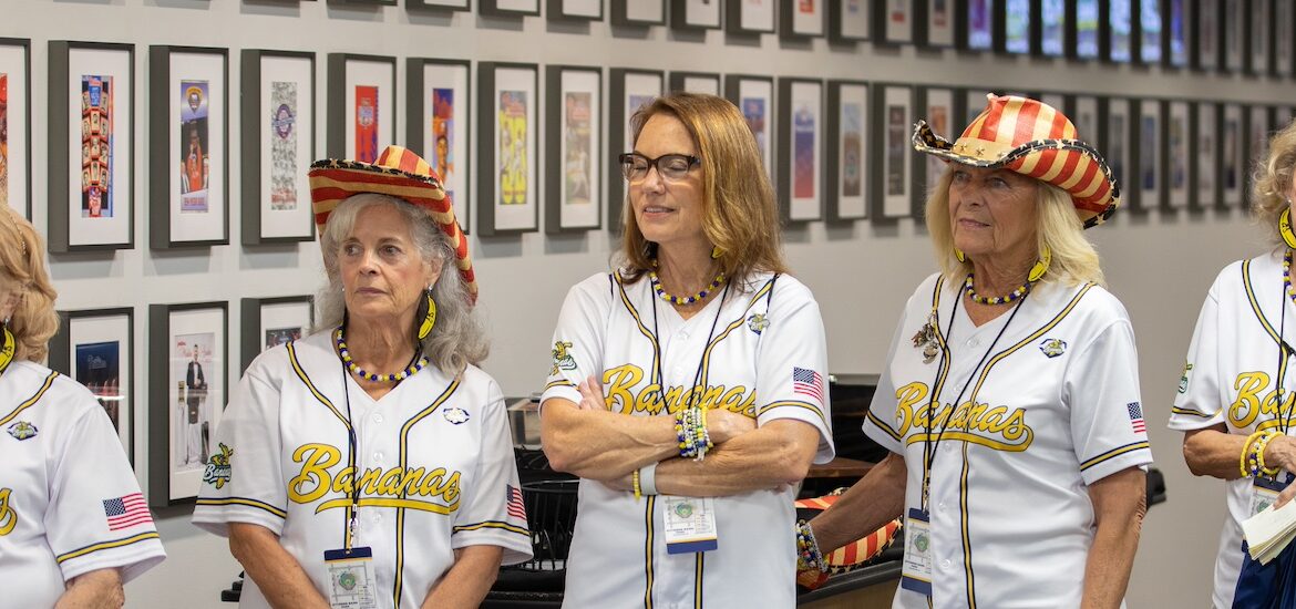 Five Banana Nanas stand shoulder to shoulder listening to a speaker before their performance.