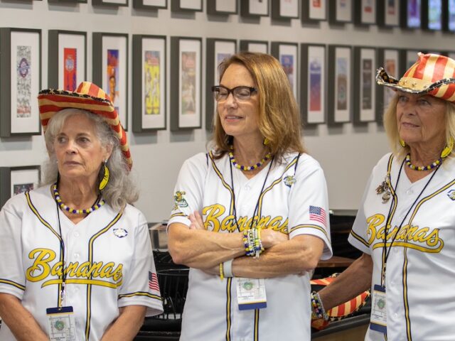 Five Banana Nanas stand shoulder to shoulder listening to a speaker before their performance.