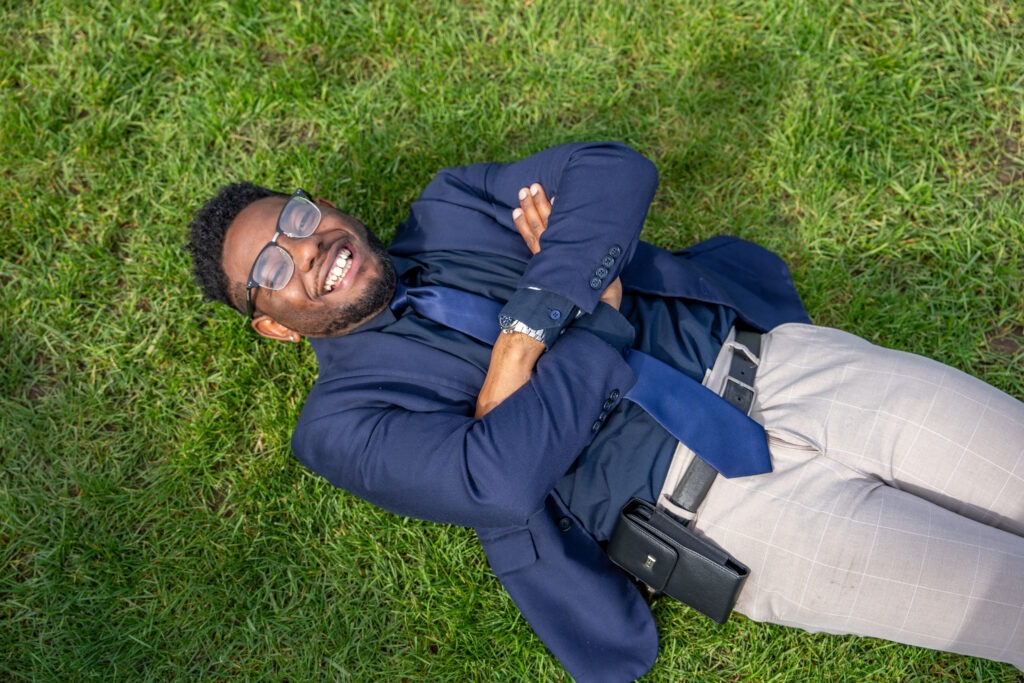 Shawn B. smiles while relaxing on campus grass, symbolizing balance and well-being as he pursues his online Doctor of Education in Educational Leadership at Rowan University.