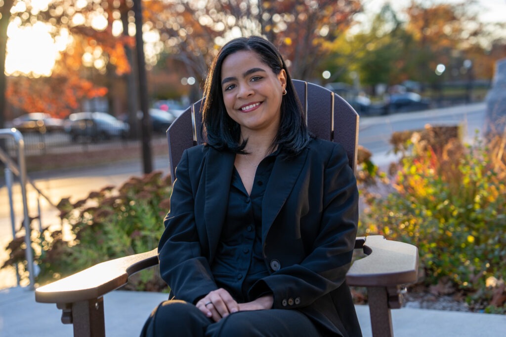 Online BA in Liberal Studies student, Flerida V., sitting outside in chair smiling with fall background.