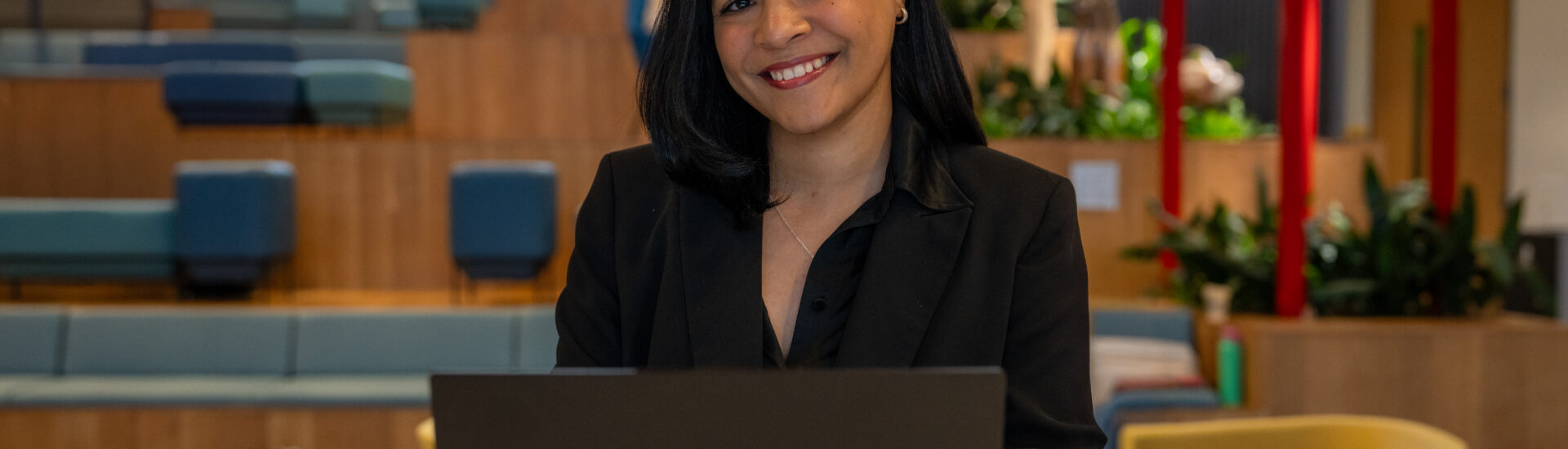 Flerida V., online BA in Liberal Studies student, sitting down at table smiling with laptop open.