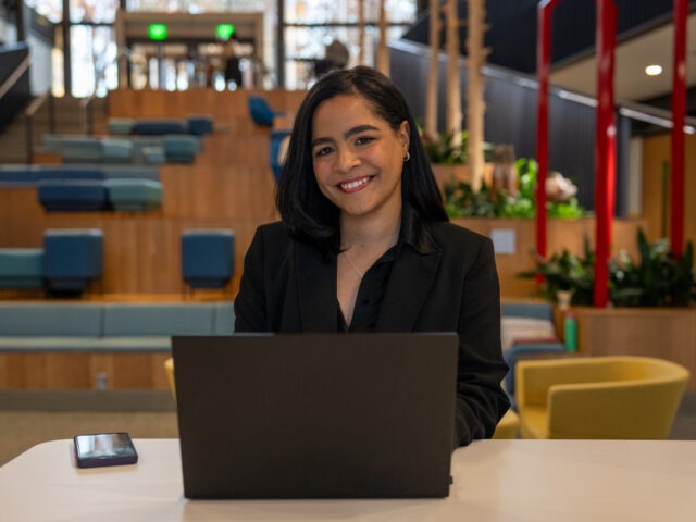 Flerida V., online BA in Liberal Studies student, sitting down at table smiling with laptop open.