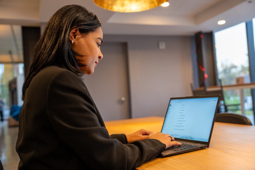 Online BA in Liberal Studies student, Flerida V., sitting down at table completing online coursework on her laptop.