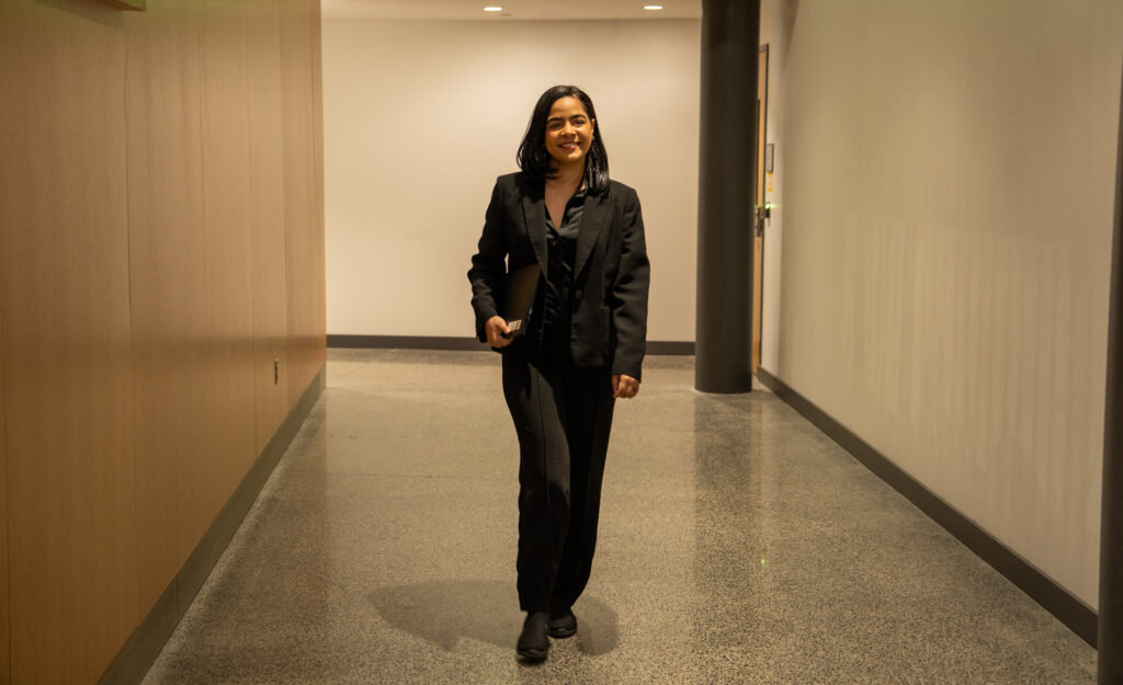 Online BA in Liberal Studies student, Flerida V., walking down hallway carrying her laptop.