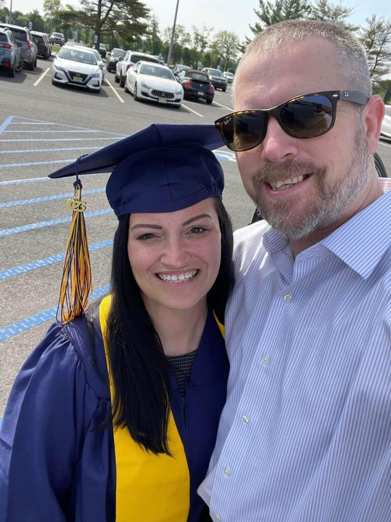 Woman wearing graduation cap and gown, smiling with male. 