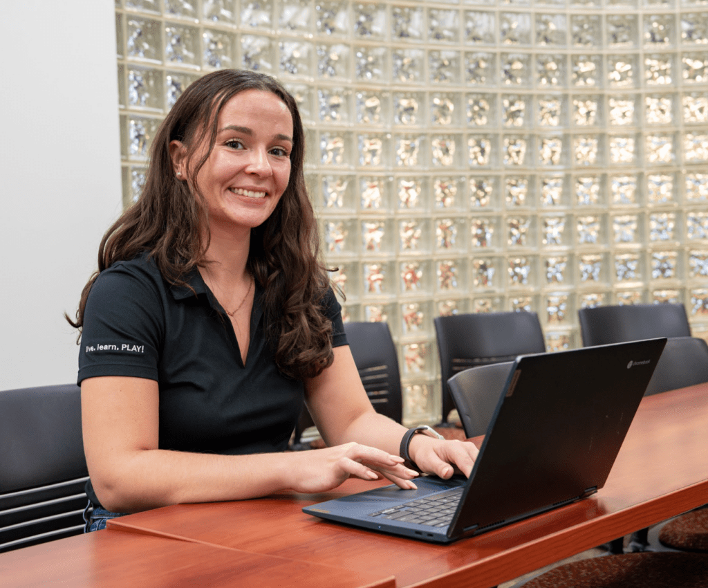 Rowan Online graduate student completing online coursework on laptop while smiling at camera.