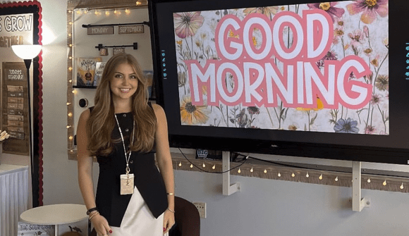 Isabella M., a Rowan University online Master of Arts in Special Education student, smiling in her classroom beside a “Good Morning” sign.